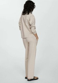 Felpa beige e pantaloni a gamba larga coordinati in tessuto morbido, con un fit rilassato e tasche laterali, visti da dietro. Sandali neri.