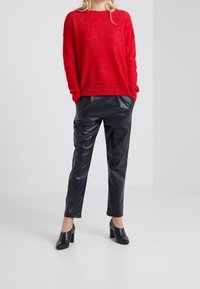 Roter gestrickter Pullover mit lockerer Passform, kombiniert mit schwarzen, glänzenden, kunstledernen, schmal geschnittenen Hosen und schwarzen, hochhackigen Schuhen.