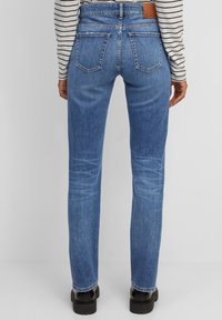 Jeans ajustados de mezclilla azul con una cintura alta, que presentan un corte de media altura, cinco bolsillos, un ligero desgastado y un parche trasero de cuero marrón.