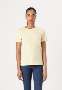 Gul bomulls t-skjorte med rund hals, korte ermer og et hvitt logo-trykk med teksten "TOMMY HILFIGER EST. 1985" på fronten.
