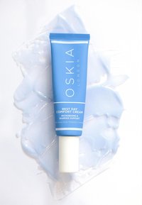 Crema Comfort Rest Day di Oskia London in un tubo blu chiaro, con tappo a vite bianco e testo che evidenzia i benefici, appoggiata su un gel blu.