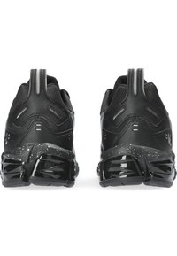 Scarpe da atletica nere con tomaia texture, dettagli riflettenti e una suola grossa a macchie bianche e nere. La vista posteriore mostra i dettagli del design.