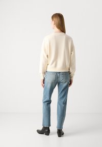 Sweatshirt couleur crème avec des épaules tombantes, associé à un jean bleu clair et des bottines noires, vu de dos sur fond blanc.