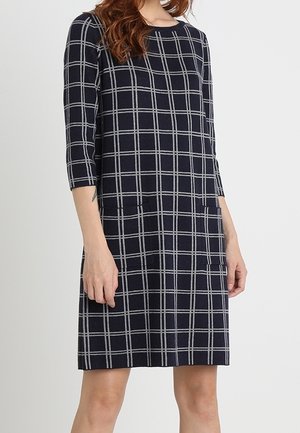 Robe bleu marine avec un motif à carreaux blancs. Elle présente des manches trois-quarts, un col rond et des poches à l'avant.