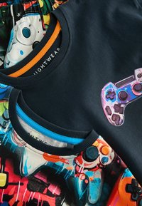 Due t-shirt sovrapposte. Una è di un blu scuro con una grafica di un controller di gioco; l'altra presenta una stampa grafica colorata.