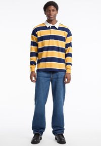Yellow and navy striped long-sleeve polo shirt with a white collar, worn with blue straight-leg jeans and black shoes.