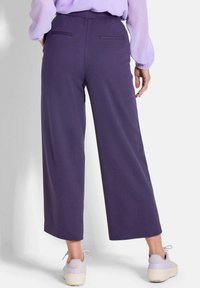 Lila weit geschnittene Hosen mit glatter Textur, ausgestattet mit Gesäßtaschen und getragen mit hellen Sneakern. Das Design hat eine entspannte Silhouette.