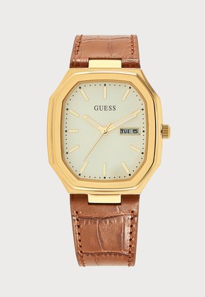 Montre-bracelet rectangulaire Guess dorée avec cadran crème, bracelet en cuir marron, index des heures et affichage jour-date indiquant mardi 5.