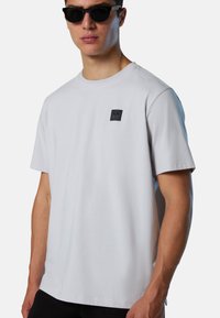 T-shirt bianco a maniche corte realizzato in cotone, con un piccolo logo patch nero sulla parte superiore del petto sinistro. Texture liscia e vestibilità rilassata.
