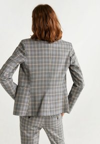 Šedý kostkovaný blazer s přiléhavým střihem, dvěma zadními ventilačními otvory a hladkou texturou, doplněný o odpovídající kostkované kalhoty.