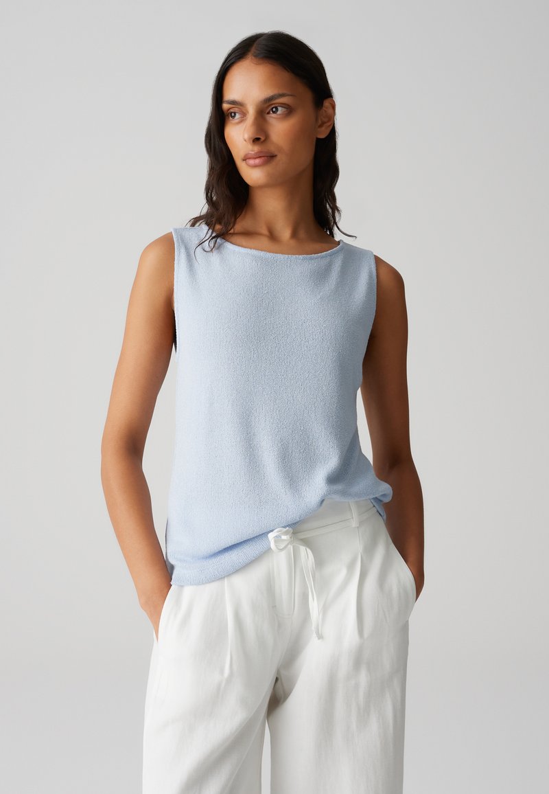 Haut sans manches bleu clair avec une finition texturée, décolleté rond et coupe décontractée, associé à un pantalon blanc ample.