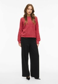 Punane tekstureeritud kootud sviiter pikkade varrukatega, kombineeritud kõrge vöökohaga mustade laiemate pükstega ja teravate mustade kontsadega. Lihtne, monokroomne disain.