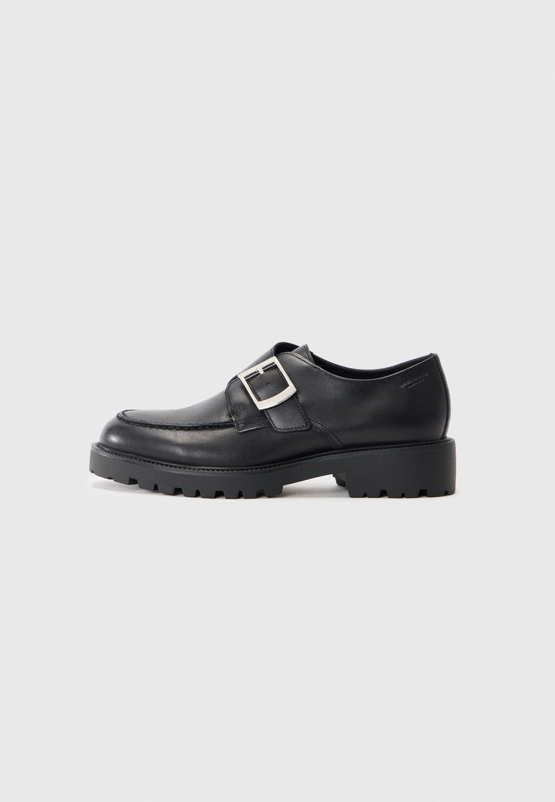Sapatos de couro pretos com bico arredondado, apresentando um detalhe de fivela na lateral e uma sola grossa e robusta. Textura suave com costuras mínimas.