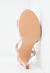 Sandale beige à talon haut montrant une semelle lisse et un talon fin sur un fond blanc en angle.