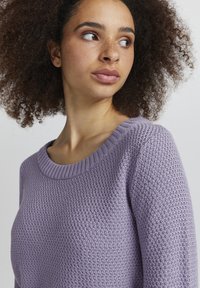 Lila gestrickter Pullover mit strukturiertem, voluminösem Muster, weitem geripptem Rundhalsausschnitt und taillierten Ärmeln. Weiches Baumwollmischgewebe.