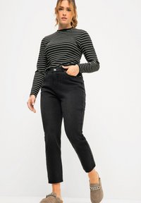 Jeans neri a vita alta con taglio dritto, abbinati a una maglia a maniche lunghe a righe bianche e nere. L'outfit include delle scarpe slip-on grigie.