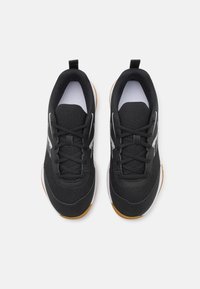 Chaussures de sport noires avec tige en maille, superpositions texturées, accents blancs et semelle en caoutchouc naturel. Elles présentent un bout rond et un design à lacets.