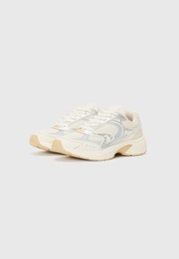 Cream-colored athletic shoes with a mesh upper, reflective accents, and beige rubber soles. Features laces and a textured design.