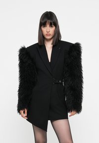Black blazer dress with exaggerated shaggy fur sleeves, featuring a cinched waist and a sleek, angular design. Smooth fabric, bold silhouette.