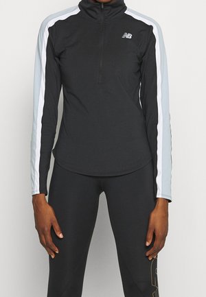 Person trägt ein schwarzes langärmliges Sportoberteil mit weißen und hellblauen Streifen an den Ärmeln und passende schwarze Leggings.
