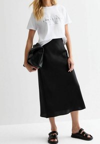 Vit T-shirt med "FRANCISCO" tryckt i grått, tillsammans med en lång svart satin kjol och svarta hängsandal. Svart texturerad clutch-väska.