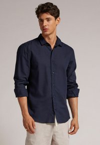 Navy Blaues Hemd aus Leinen mit einer weichen Textur. Verfügt über lange Ärmel, die an den Manschetten hochgerollt sind, und ein klassisches Kragen-design.