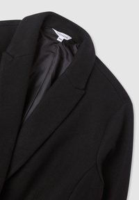 Cappotto in lana nera su misura con colletto a revers e rivestimento interno liscio, taglia 2XL, esposto su uno sfondo grigio chiaro.