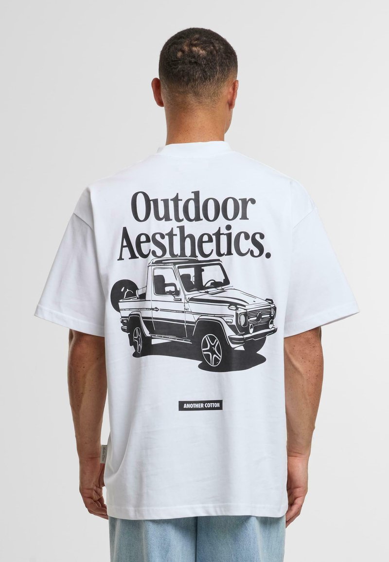 Camiseta de algodón blanca con mangas cortas, que presenta un gráfico negro de un vehículo y el texto "Estética al aire libre". Etiqueta de la marca en la parte inferior.