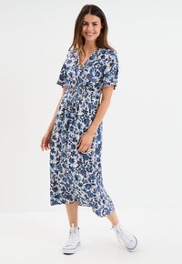 Blau-weißes florales Midikleid mit kurzen Ärmeln und V-Ausschnitt, ausgestattet mit einer taillierten Taille und einem luftigen Rock, kombiniert mit weißen Sneakers.