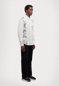 Cămașă cu mâneci lungi, alb-negru cu dungi, prezentând desene grafice, asortată cu pantaloni negri și adidași alb-negru. Ajustare simplă și modernă.
