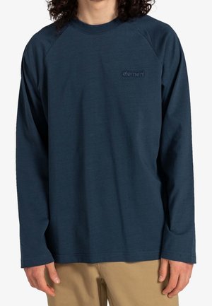 Person trägt ein dunkelblaues Langarmshirt mit dem "element"-Logo auf der Brust und hellbraune Hosen, steht vor einem weißen Hintergrund.