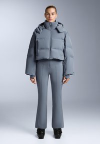 Sivi puffer jakna s visokim ovratnikom i skraćenim dizajnom, uparen s pripijenim sivim hlačama na zvono; glatka tekstura, bez vidljivih uzoraka.