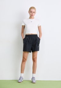 Black athletic shorts with a drawstring waist, two zippered pockets, and green accent detail paired with a white cropped t-shirt.