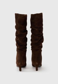 Knee-high brown suede boots with a slouchy design, tapered shape, and a small heel, featuring a soft texture and no visible hardware.