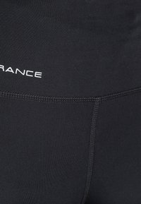 Svarta atletiska leggings med en slät, stretchig tyg, platta sömmar och märkestext. Designen inkluderar en hög midja för stöd.