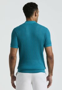 Turqouise polo shirt met korte mouwen, voorzien van een gestructureerd ruitpatroon, ribgebreide kraag en manchetten, getailleerd ontwerp en een contrasterende effen band rond de taille.