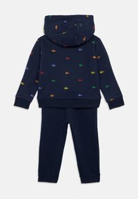 Tums zila bērnu kapuce un bikses komplekts ar daudzkrāsaini maziem krokodilu logotipiem, kas izklāta uz augšdaļas.