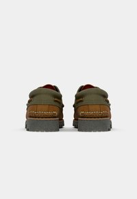 Braune und grüne Schuhe mit gepolstertem Kragen, Obermaterial aus braunem Leder, geflochtenen Nähten, Gummisohle und metallischen Akzenten an den Seiten.