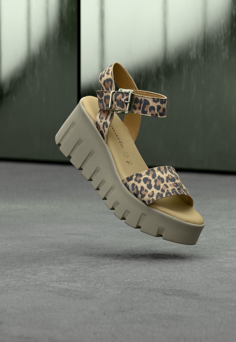 Sandale à plateforme imprimé léopard avec semelle beige épaisse et crantée, et bride de cheville avec boucle argentée sur fond de sol gris.