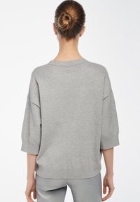 Hellgrauer Oversize-Pullover mit kurzen Ärmeln, gerippten Bündchen und weitem Ausschnitt. Hergestellt aus weichem, strukturiertem Strickmaterial.