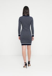 Vestito a maglia a fantasia navy con maniche lunghe e polsini a coste, lunghezza a metà coscia, abbinato a sandali neri con tacco alto.