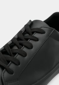 Must have musta nahast tossud, millel on lamedad mustad paelad, sile pind ja minimalistlik disain ümmarguse varba ning diskreetse õmblusdetailiga.