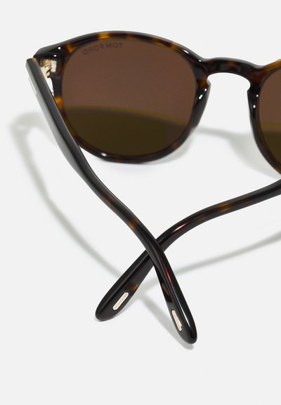 Ochelari de soare tortoise maro cu un design rotund, lentile întunecate și brațe negre elegante, cu mici accente metalice.