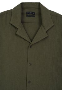 Camicia verde oliva, texturizzata, con una vestibilità comoda, caratterizzata da un colletto a punta, bottoni frontali e pieghe sottili per un aspetto informale.
