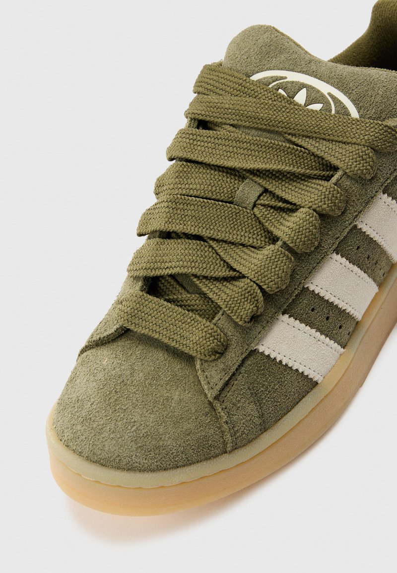 Sneaker in suede verde oliva con accenti a strisce bianche, punta rotonda, lacci spessi e testurizzati, e suola in gomma naturale.
