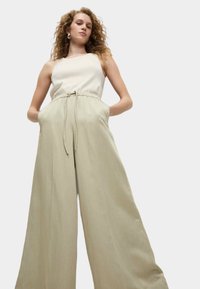 Helle beigen weit geschnittene Hose mit hohem Bund, Kordelzugverschluss und Seitentaschen, aus einem weichen, strukturierten Stoff.