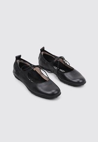 Bailarinas de cuero negro con punta redondeada, lados recortados y un fino detalle de cordón. Parte superior texturizada y suelas lisas.