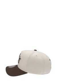 Casquette de baseball crème et marron avec une visière plate, présentant des détails de couture et des trous de ventilation sur les côtés. Logo brodé à l'avant.