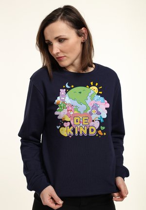Marineblå sweatshirt med et farverigt grafisk design af tegneserie-bjørne, en globe og teksten "VÆR VENLIG", med rund hals og lange ærmer.