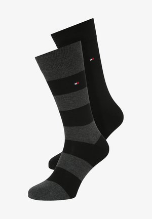 Deux paires de chaussettes en coton : l'une est noire uni, l'autre est grise avec des rayures horizontales noires. Chacune arbore un petit logo sur le revers.